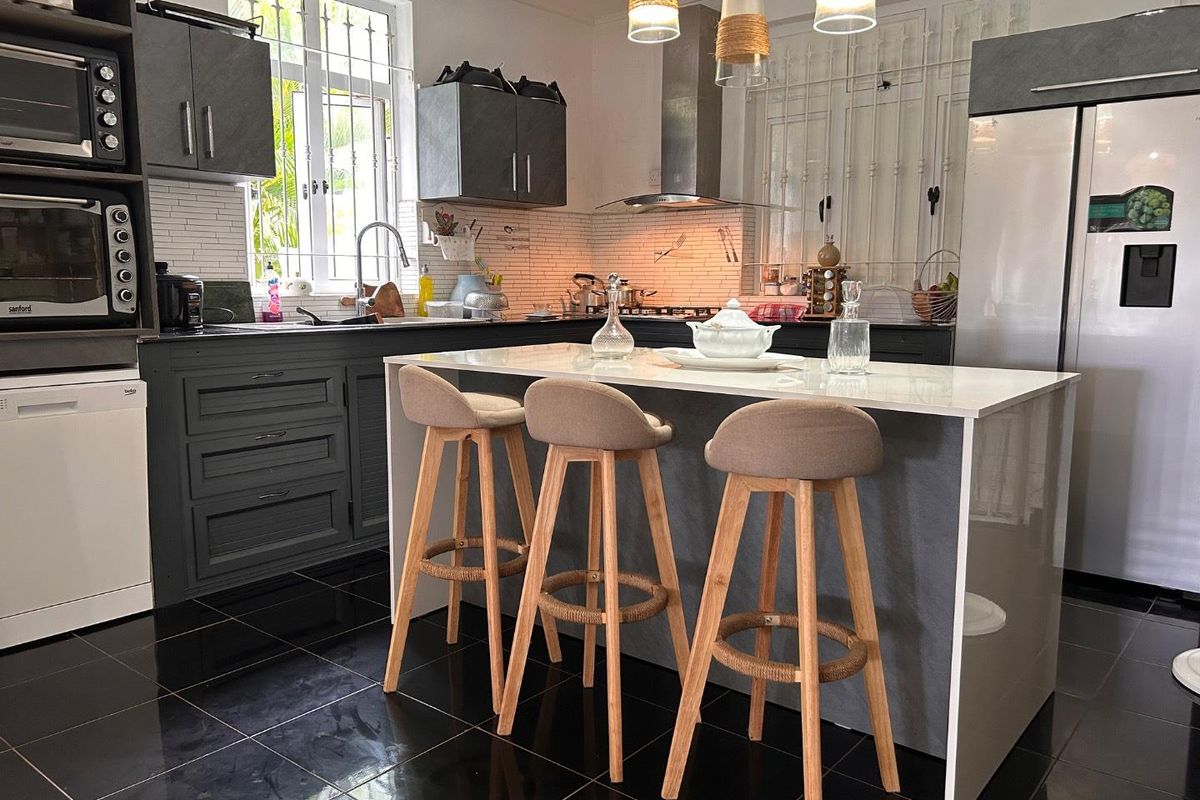 Modern kitchen featuring dark cabinetry, a central island with breakfast bar seating, stainless steel extractor fan, and tiled backsplash.