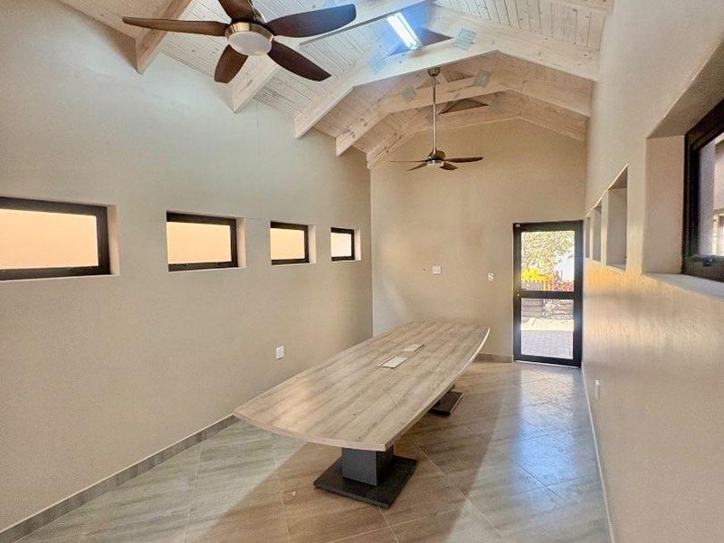 Modern office space featuring a high vaulted timber ceiling with exposed trusses, skylights, ceiling fans, and a large built-in boardroom table.