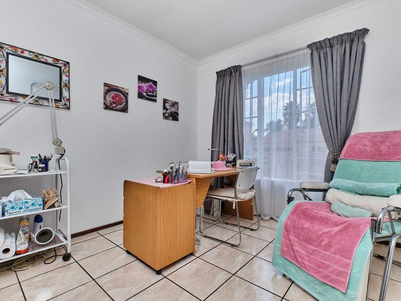 A functional bedroom space currently utilized as a beauty treatment room, featuring tiled flooring and natural light through a window with curtain rails.