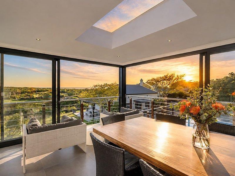 A modern covered balcony featuring large sliding glass doors, a skylight, and panoramic sunset views over the surrounding landscape.