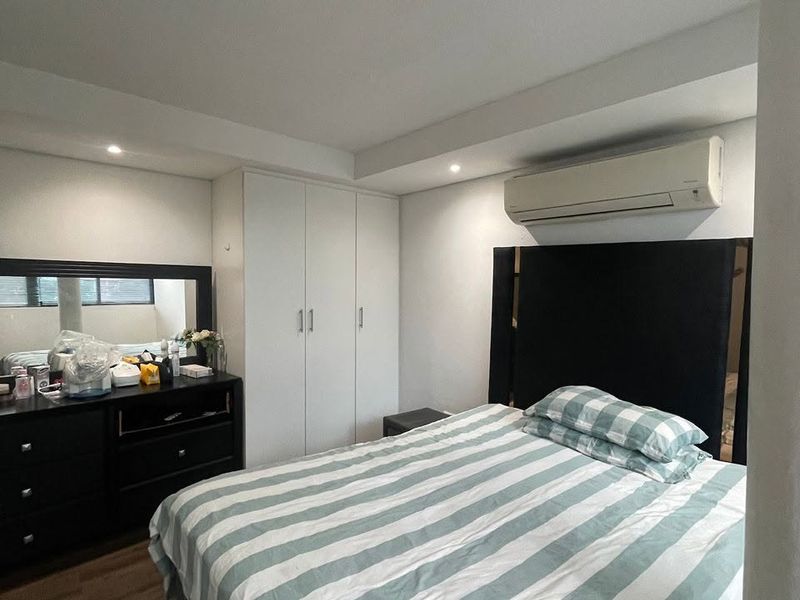 A well-maintained bedroom featuring built-in wardrobes, laminate flooring, recessed lighting, and a wall-mounted split-system air conditioning unit.