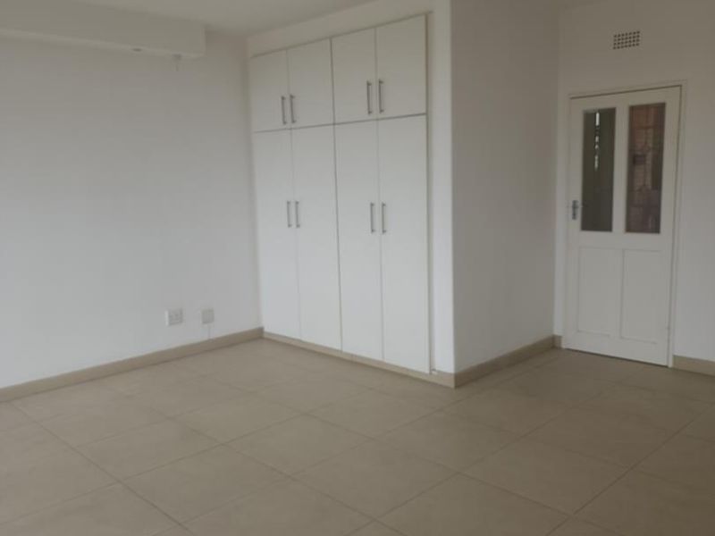 A clean, empty bedroom featuring neutral tiled flooring, white built-in cupboards, and a standard internal door, offering a blank canvas for personalization.