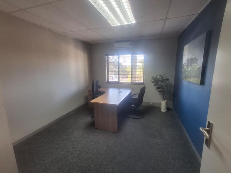 A functional office space featuring carpeted flooring, a suspended ceiling with integrated lighting, and a wall-mounted air conditioning unit.