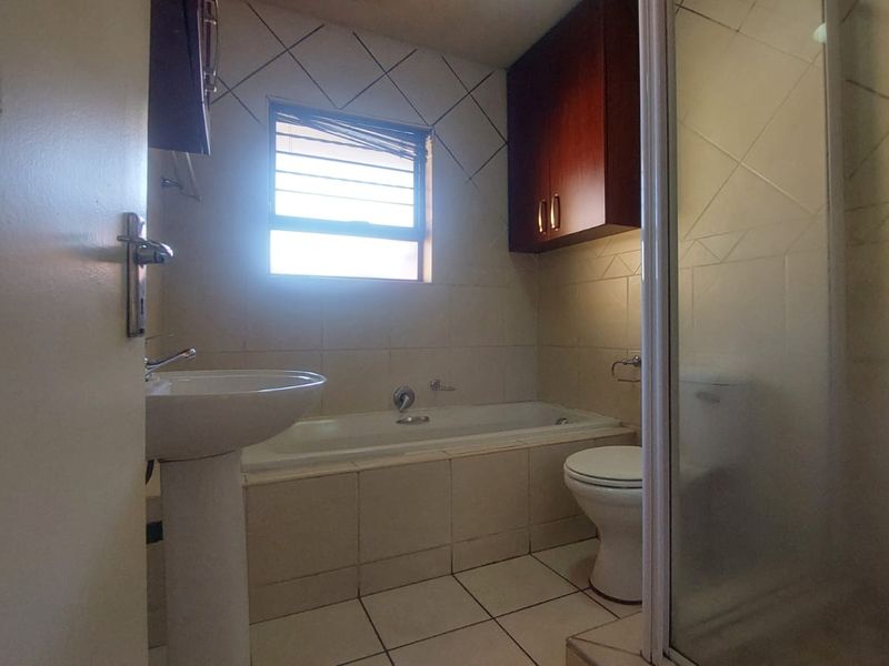 A functional bathroom featuring a pedestal basin, built-in bathtub, toilet, and a separate shower enclosure with tiled finishes throughout.