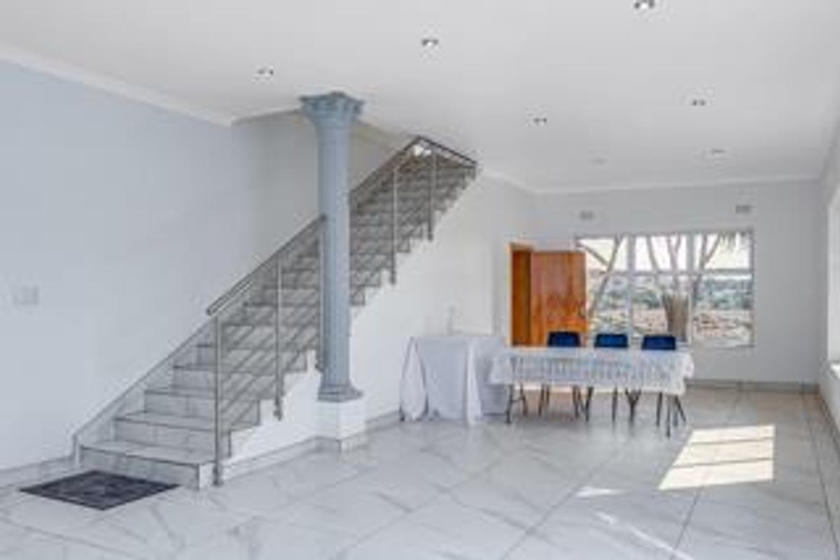 Spacious open-plan living area featuring modern porcelain floor tiles, a striking staircase with stainless steel balustrades, and abundant natural light.