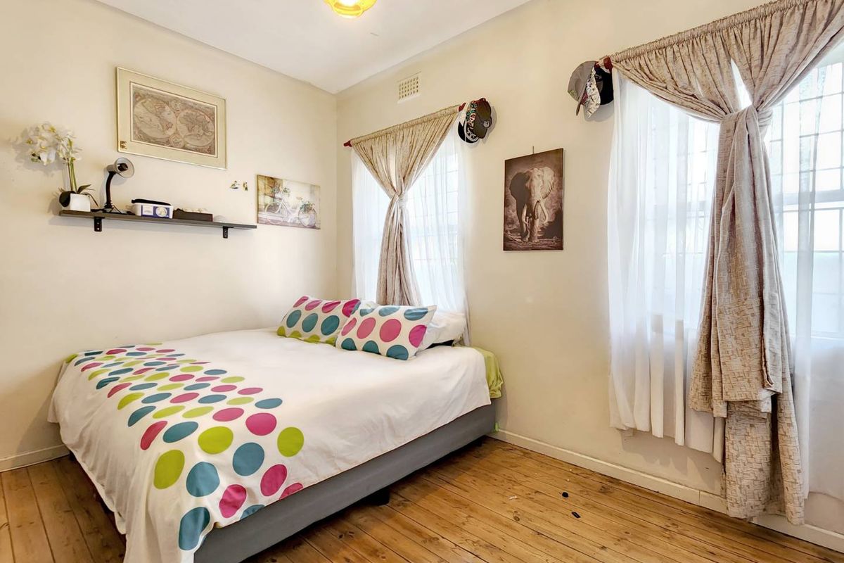 A bedroom featuring original timber flooring, dual windows with curtains, and a central ceiling light fixture.