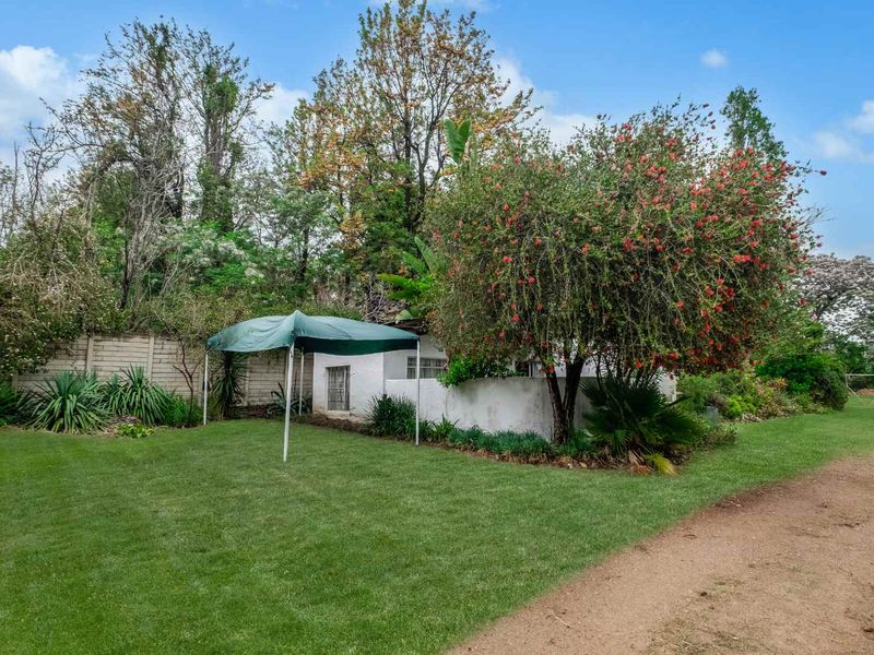 A well-maintained garden area featuring a lush lawn, mature trees, and a precast concrete boundary wall on a farm property.