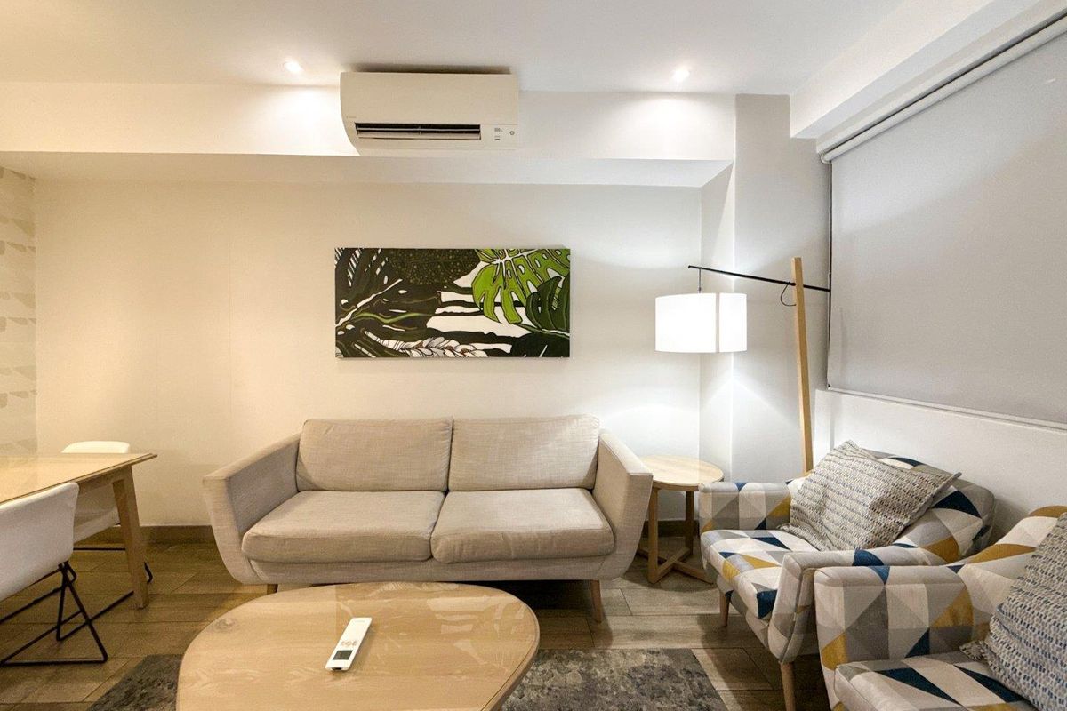 A well-maintained living area featuring recessed ceiling lighting, a wall-mounted air conditioning unit, and neutral tiled flooring.
