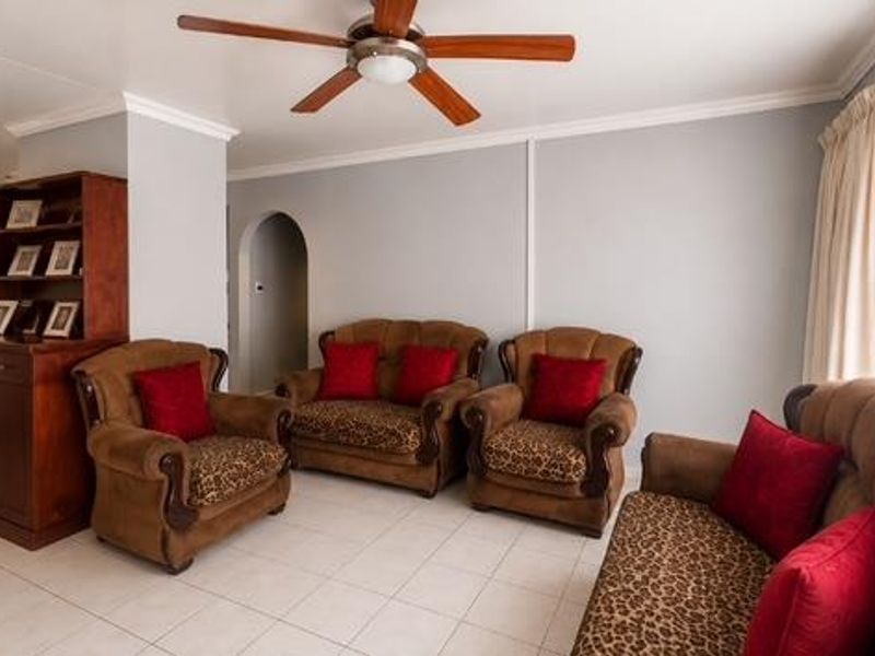 A spacious living room featuring tiled flooring, a ceiling fan, and an arched entryway leading to adjacent living areas.