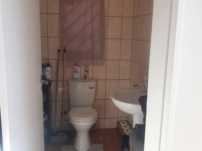 A compact bathroom featuring ceramic wall and floor tiles, a pedestal washbasin, and a standard toilet.