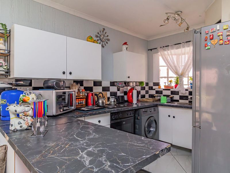 Functional kitchen featuring dark marble-effect countertops, white cabinetry, black and white tiled backsplash, and integrated laundry appliance space.
