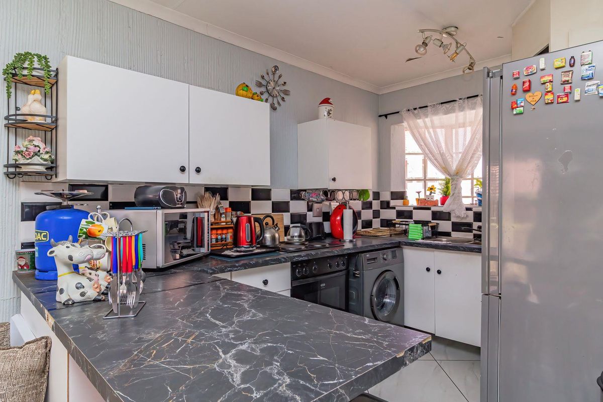 Functional kitchen featuring dark marble-effect countertops, white cabinetry, black and white tiled backsplash, and integrated laundry appliance space.