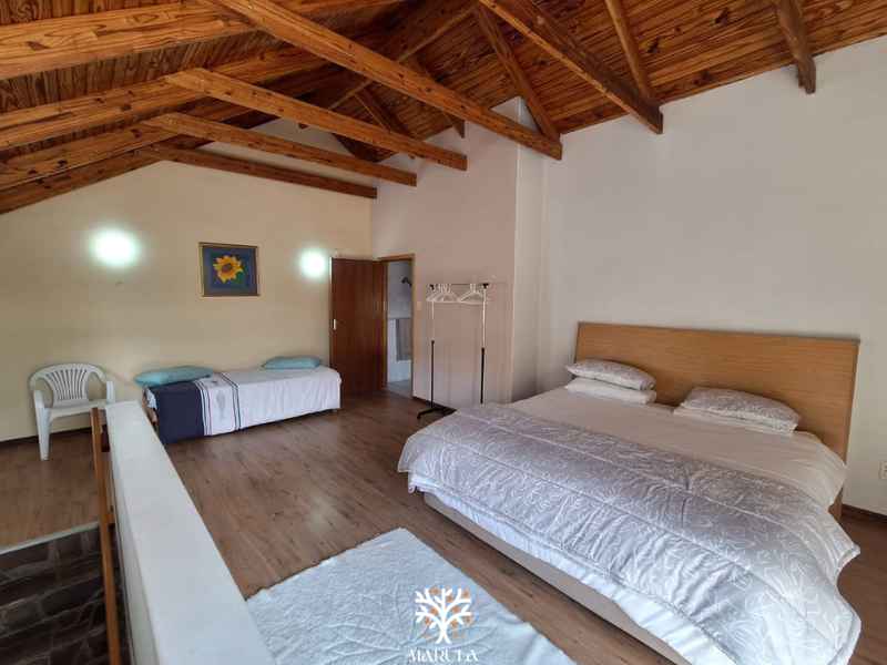 Spacious bedroom featuring high vaulted ceilings with exposed timber trusses and laminate flooring, offering a rustic and airy atmosphere.