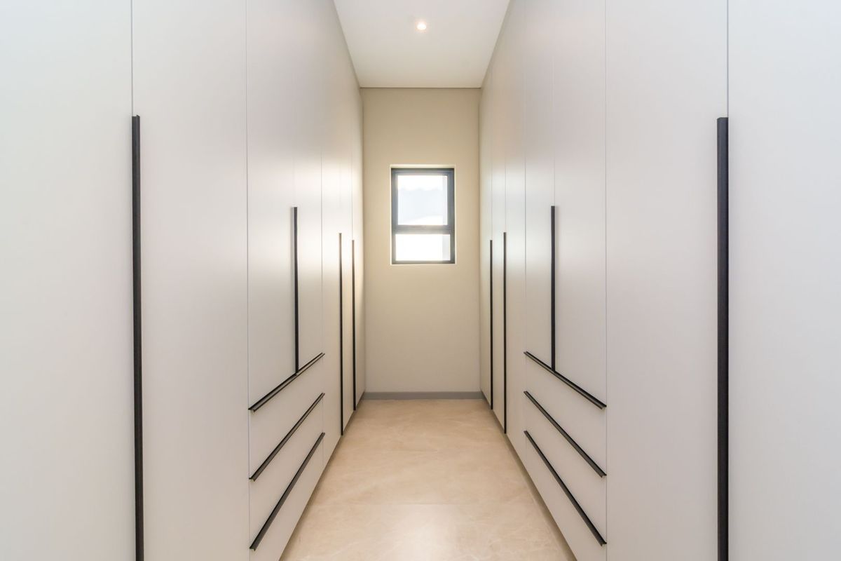 A modern walk-in closet or dressing area featuring extensive floor-to-ceiling built-in cabinetry with sleek black handles and neutral tiled flooring.