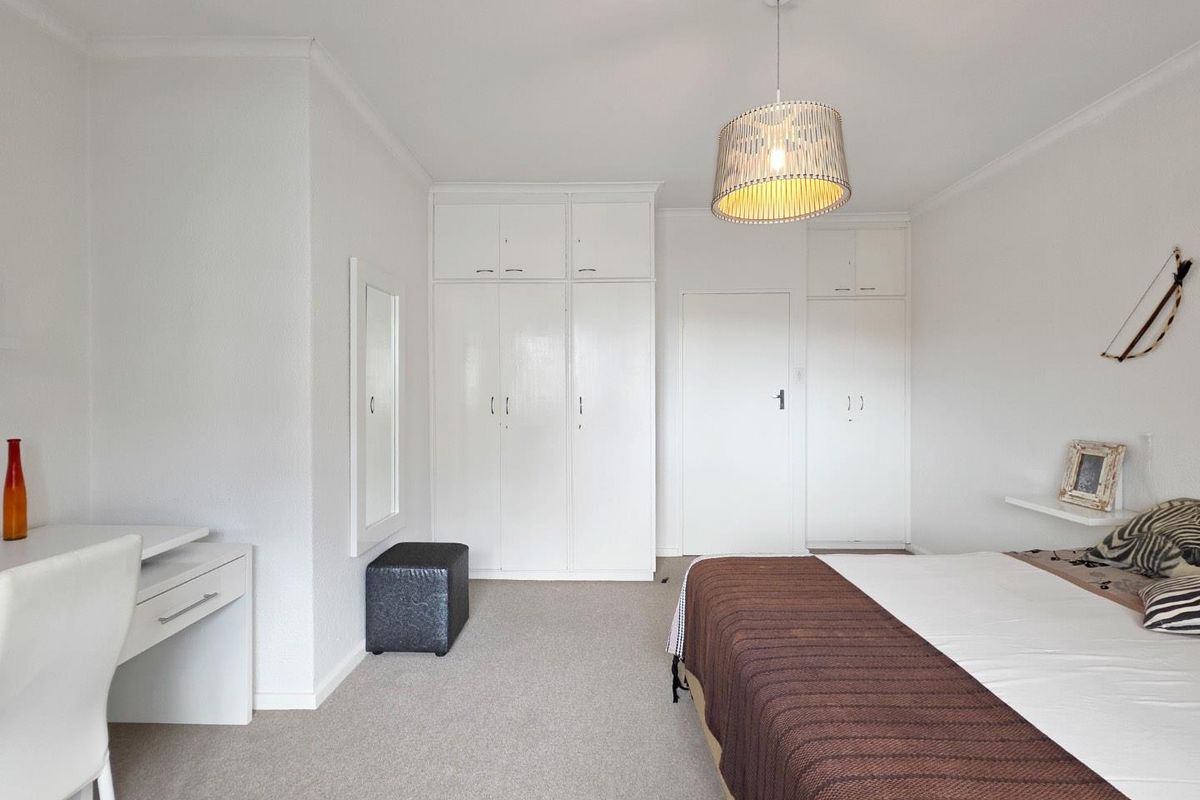 A bedroom featuring neutral carpeted flooring, built-in white cupboards, and a central pendant light fixture.