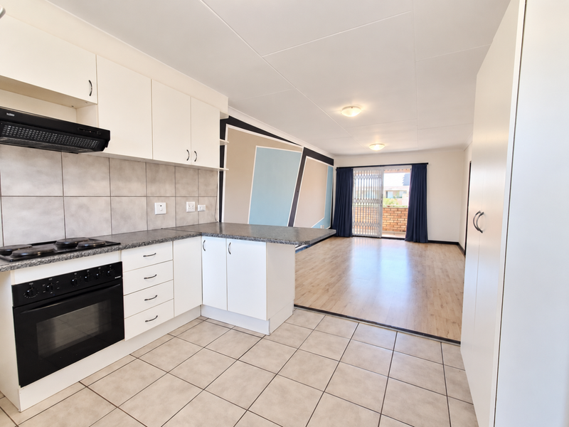 Spacious open-plan kitchen and living area featuring modern cabinetry, built-in appliances, laminate flooring, and direct access to a balcony through sliding doors.