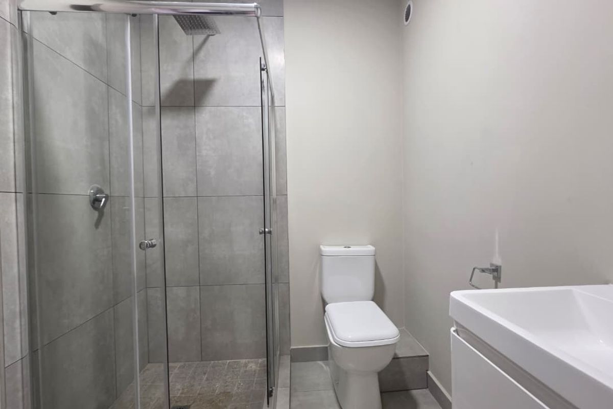 Modern bathroom featuring a walk-in shower with glass screen, rain shower head, contemporary toilet, and a sleek vanity basin with tiled finishes.
