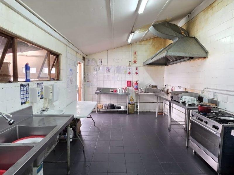 A functional commercial kitchen space featuring stainless steel sinks, a gas stove, and a commercial extractor hood with tiled surfaces throughout.