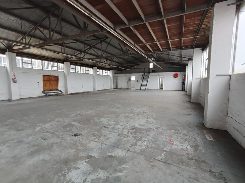 Spacious industrial warehouse unit featuring high ceilings with exposed steel trusses, concrete flooring, and natural light through large industrial windows.