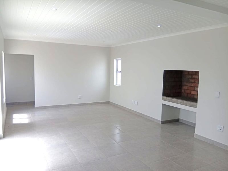 Spacious, empty living area featuring neutral tiled floors, a built-in brick fireplace, and a clean tongue and groove ceiling with recessed lighting.