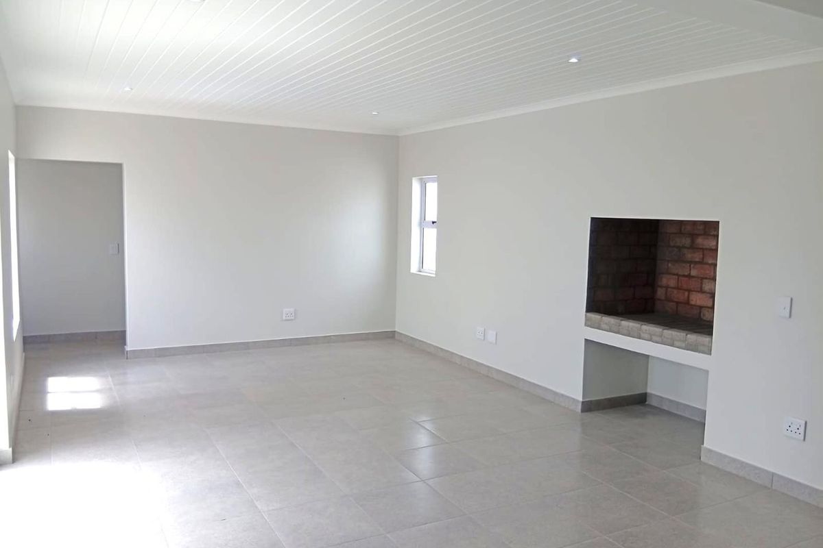 Spacious, empty living area featuring neutral tiled floors, a built-in brick fireplace, and a clean tongue and groove ceiling with recessed lighting.