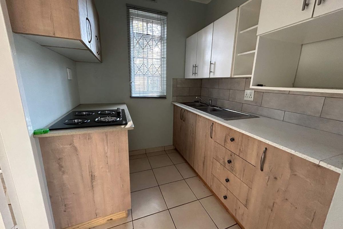 A functional kitchen featuring wood-look cabinetry, laminate countertops, a built-in electric hob, and a double bowl sink with tiled backsplash.