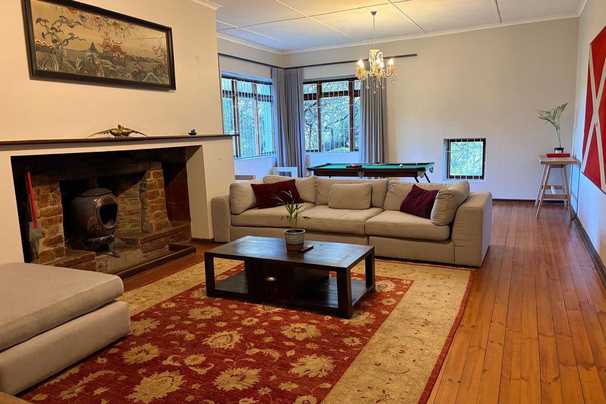 Spacious living room featuring a rustic brick fireplace with a wood-burning stove, polished timber flooring, and large windows providing natural light.