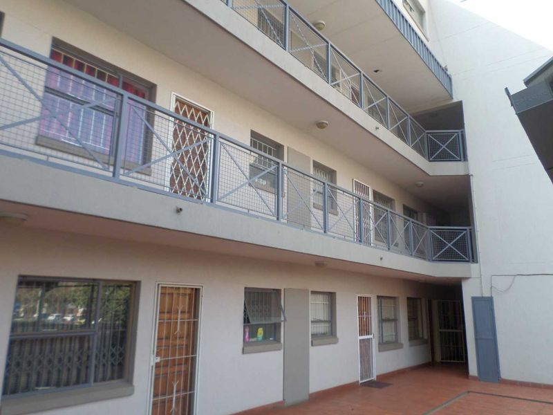 Exterior view of an apartment building featuring multi-level walkways with metal security railings and security-gated access points.