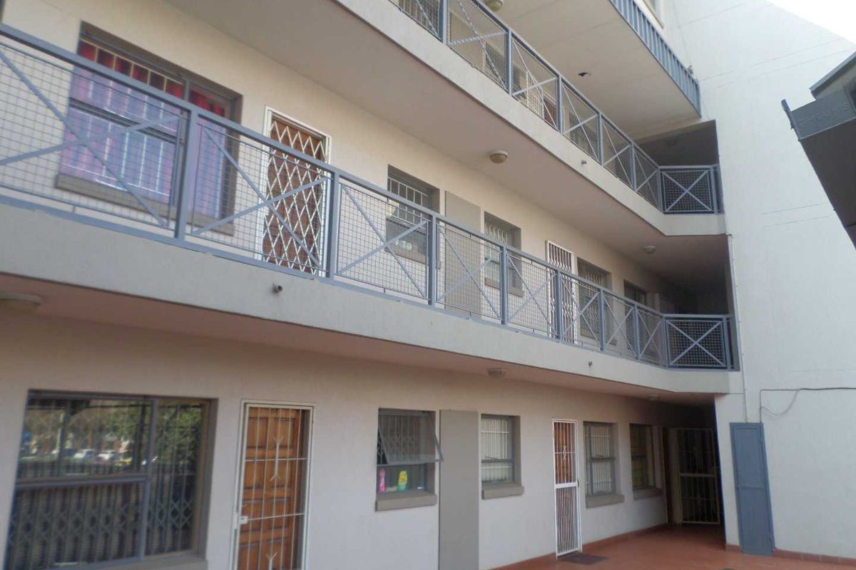 Exterior view of an apartment building featuring multi-level walkways with metal security railings and security-gated access points.