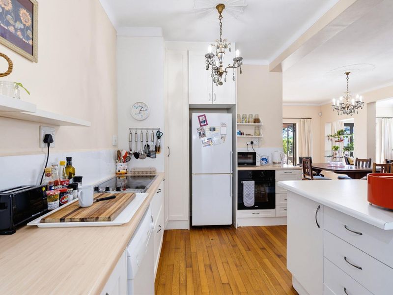 A functional kitchen featuring hardwood flooring, built-in cabinetry, an electric hob, and an integrated oven, flowing into an adjacent dining area.
