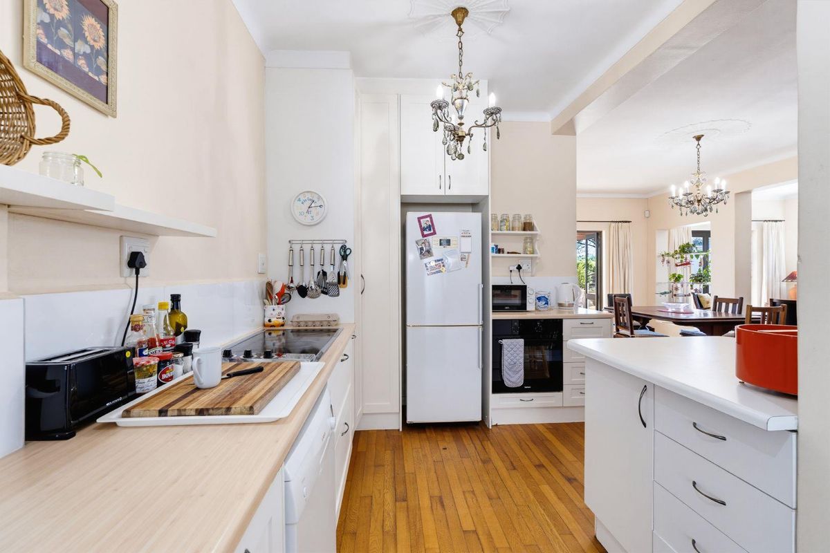 A functional kitchen featuring hardwood flooring, built-in cabinetry, an electric hob, and an integrated oven, flowing into an adjacent dining area.