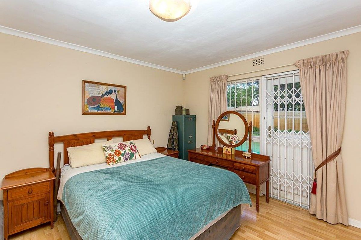 A well-lit bedroom featuring laminate flooring, a ceiling light fixture, and a sliding door with a security gate providing access to the exterior.