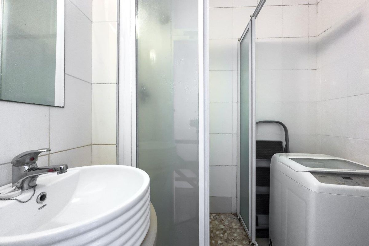 A functional bathroom featuring a white ceramic basin, a shower enclosure, and tiled wall finishes, providing essential utility space.