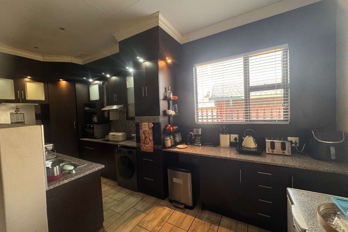 A functional kitchen featuring dark wood cabinetry, granite countertops, built-in oven, extractor fan, and tiled flooring with ample natural light.