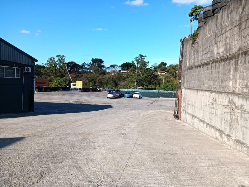 Spacious industrial concrete yard featuring a large retaining wall and adjacent warehouse building, suitable for logistics or storage operations.