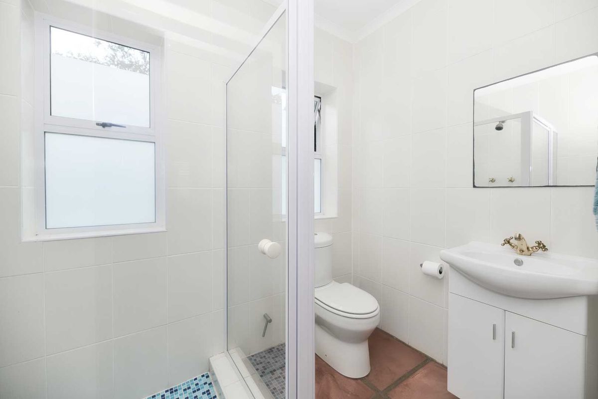 A clean, bright bathroom featuring a glass-enclosed shower with mosaic tiling, a white vanity, and a modern toilet.