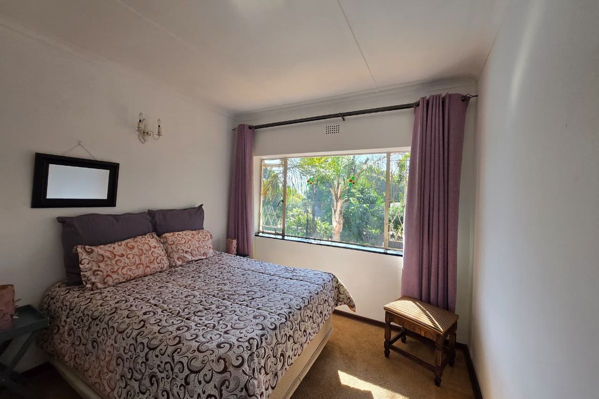 A bedroom featuring a large window with garden views, carpeted flooring, and wall-mounted lighting fixtures.