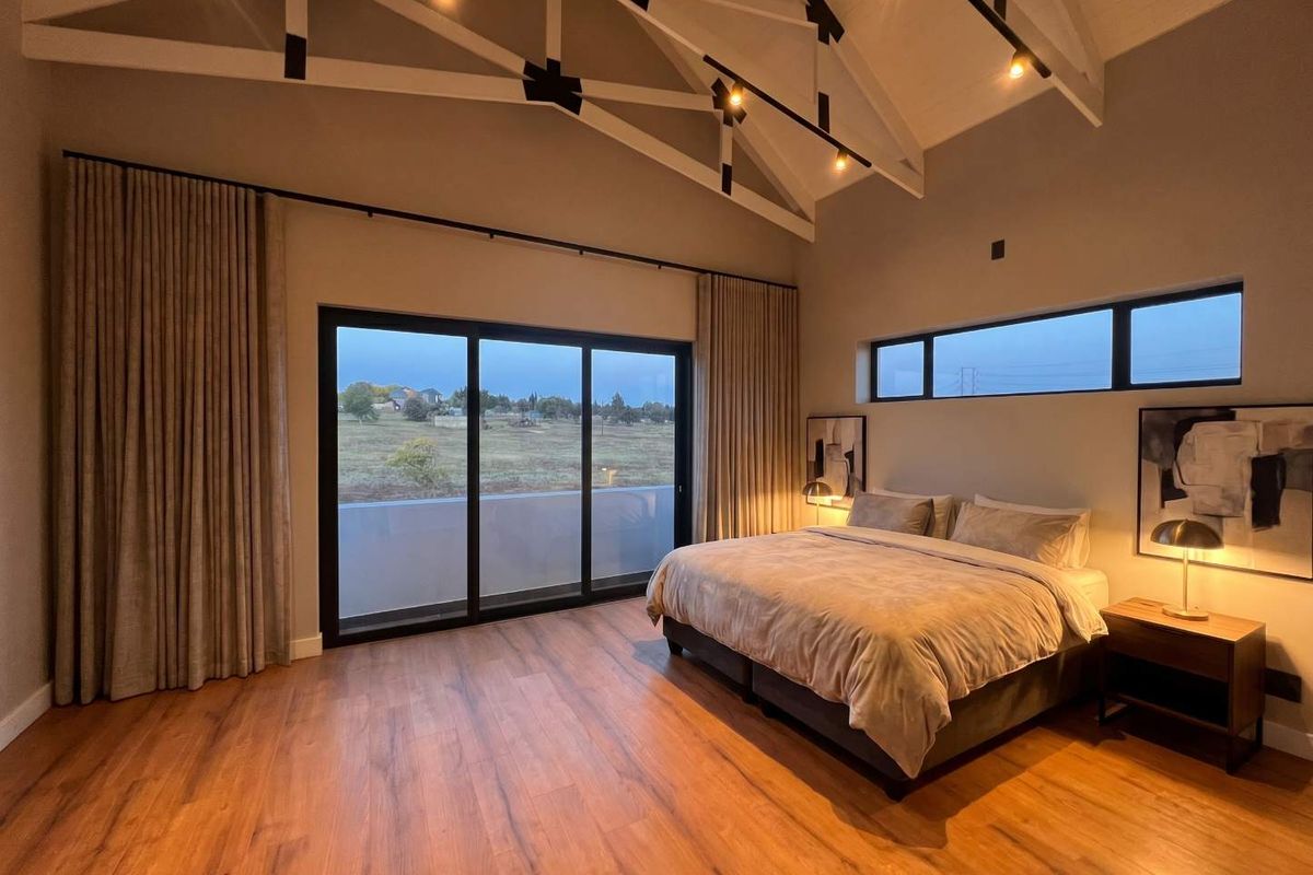 Spacious bedroom featuring high vaulted ceilings with exposed trusses, large sliding doors leading to a balcony, and modern clerestory windows.