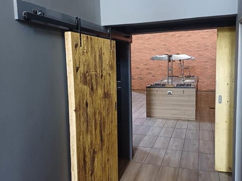 A functional kitchen area featuring a central island with built-in cooktops, extractor hoods, and a rustic sliding barn door entrance.
