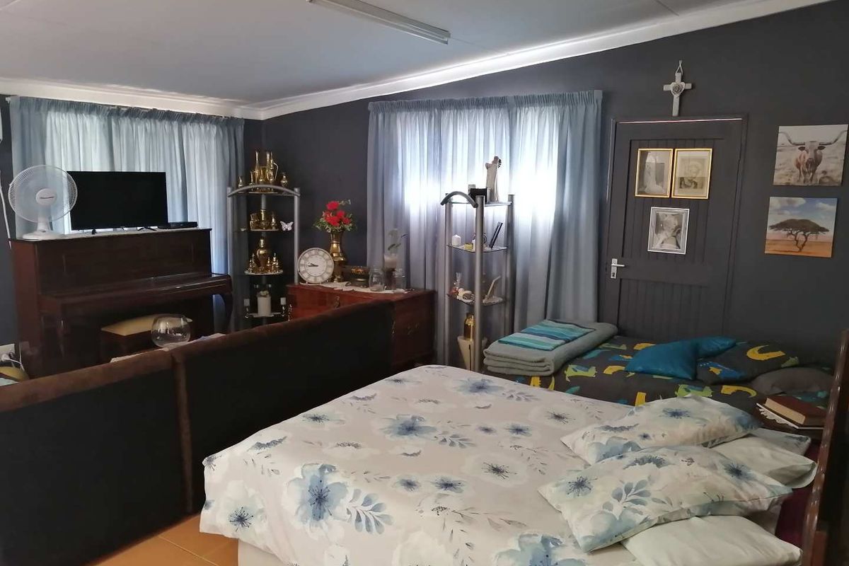 A spacious bedroom featuring dark painted walls, tiled flooring, and large windows with curtains, providing a functional living space.