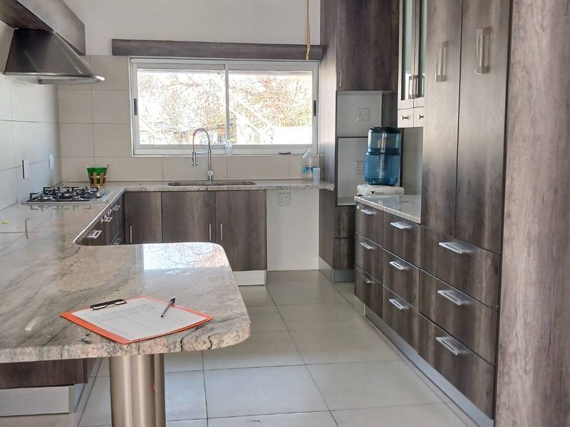 Modern kitchen featuring dark wood-grain cabinetry, stone countertops, a gas hob with extractor fan, and tiled flooring.