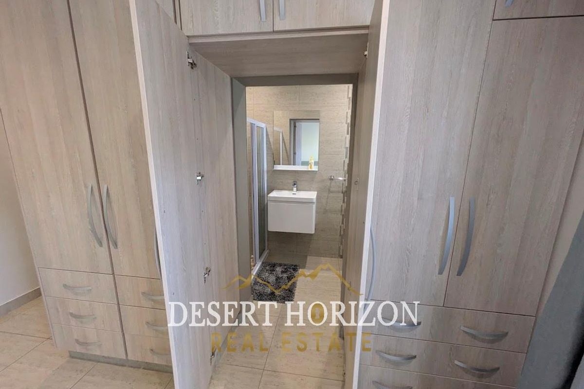 A dressing area featuring extensive built-in cabinetry with light wood-grain finish, leading directly into a modern en-suite bathroom with a wall-mounted vanity.