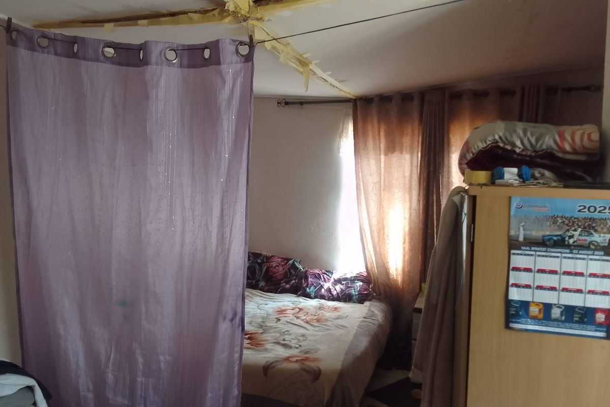 A bedroom space featuring a partitioned area with visible ceiling damage and exposed insulation, requiring significant maintenance and repair.