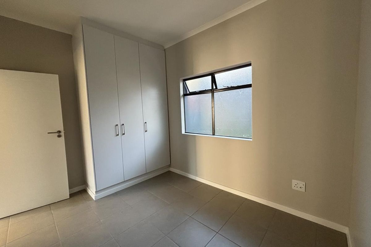 A clean, empty bedroom featuring neutral tiled flooring, built-in cupboards, and a window providing natural light.
