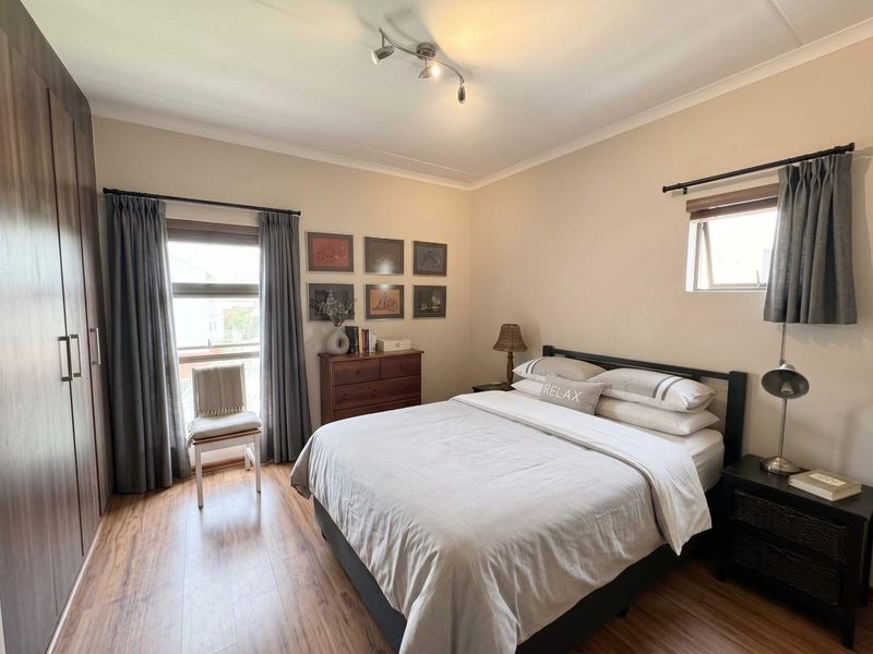 A well-maintained bedroom featuring laminate flooring, built-in cupboards, and natural light from dual windows.