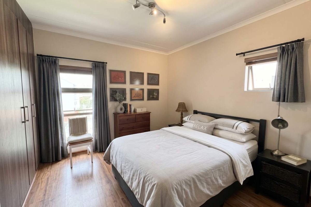 A well-maintained bedroom featuring laminate flooring, built-in cupboards, and natural light from dual windows.