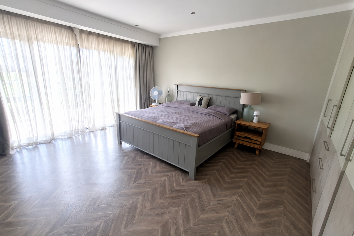 Spacious bedroom featuring modern herringbone flooring, recessed lighting, and extensive built-in cupboard storage, complemented by large windows with elegant sheer curtains.