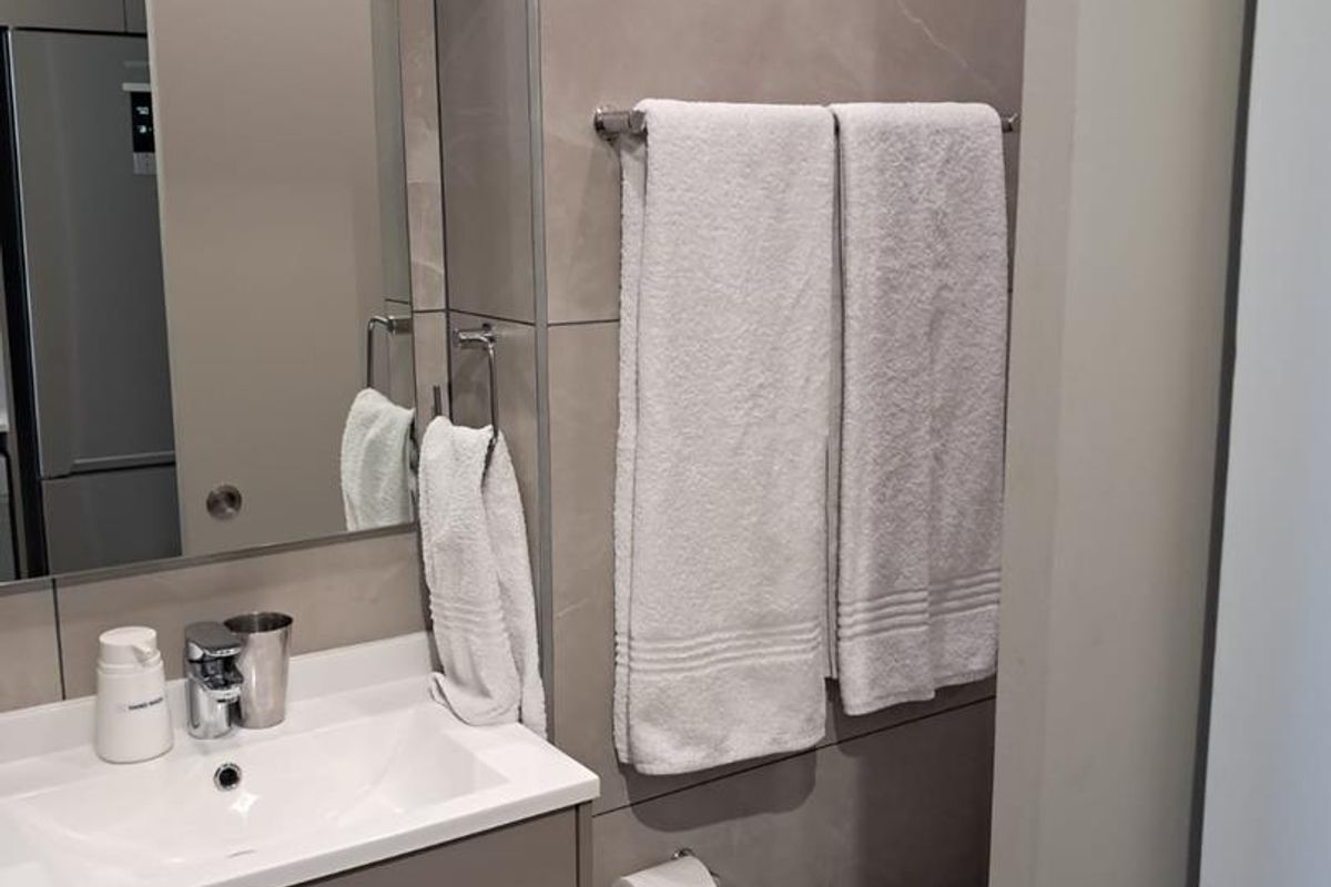 A modern, well-maintained bathroom featuring a sleek vanity cabinet, integrated sink, large wall mirror, and contemporary large-format ceramic wall tiling.
