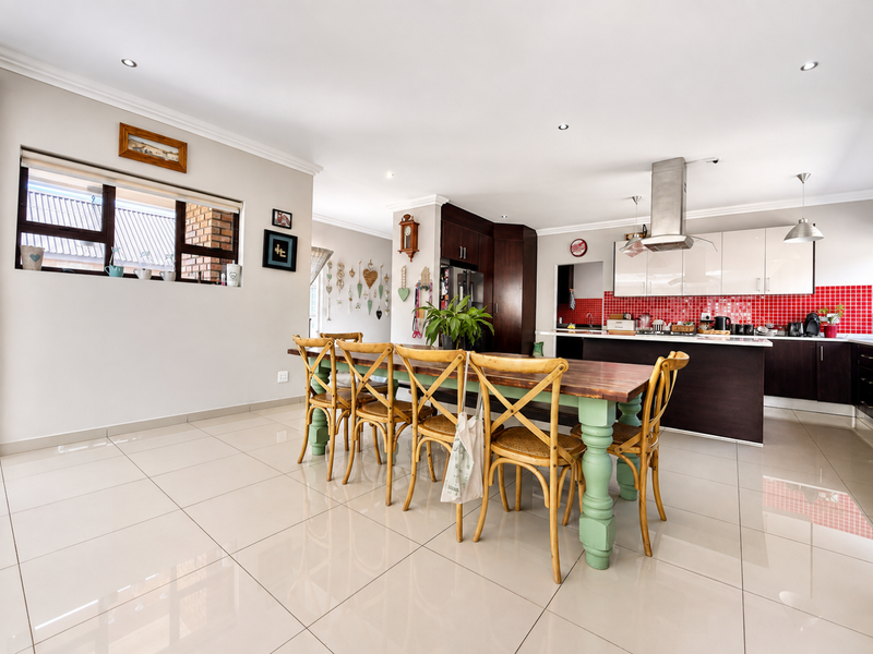 Spacious open-plan kitchen and dining area featuring modern tiled floors, a central island, and a vibrant red mosaic tile backsplash.