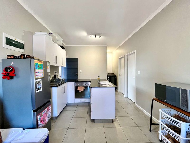 Modern kitchen featuring white cabinetry, dark stone countertops, integrated oven and hob, and neutral tiled flooring in an open-plan layout.